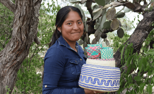 Mujer artesana zapoteca sonriendo con una canasta de palma tejida a mano en la Sierra Sur de Oaxaca